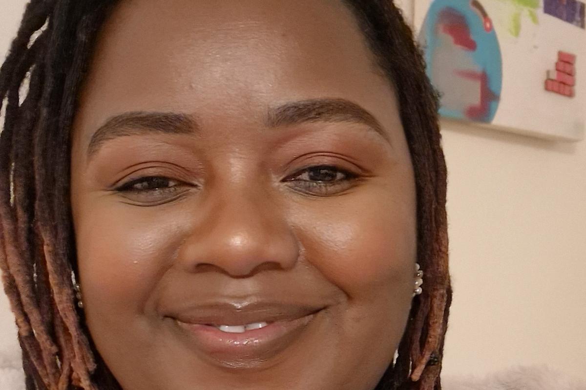 Tatenda smiling in a brown top sitting down