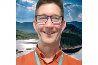 A man wearing an orange top smiles at the camera